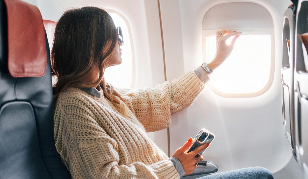 Frau-sitzt-im-Flugzeug-und-benutzt-Sonnenblende Frau-sitzt-im-Flugzeug-und-benutzt-Sonnenblende