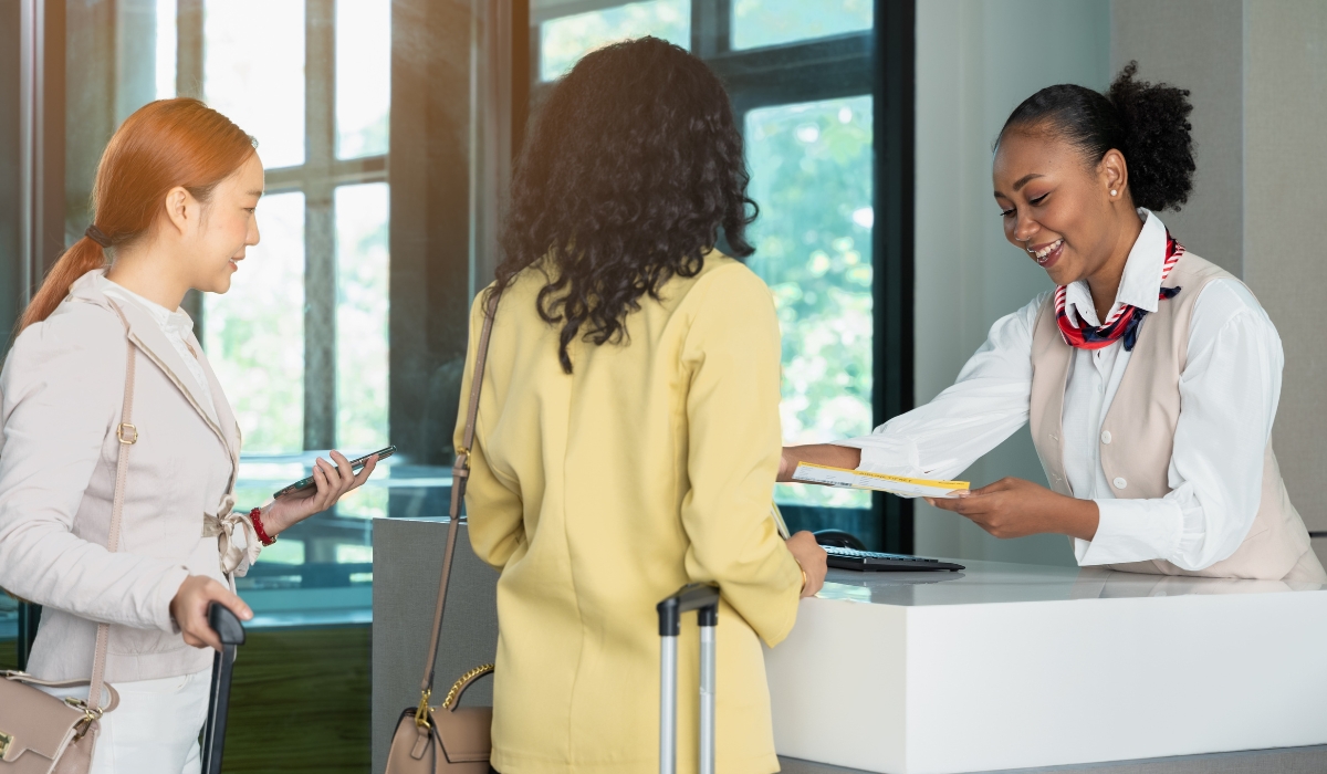 Zwei-Frauen-stehen-am-Flughafen-beim-Boarding-und-uebergeben-Boardingpass-an-Mitarbeiter Zwei-Frauen-stehen-am-Flughafen-beim-Boarding-und-übergeben-Boardingpass-an-Mitarbeiter