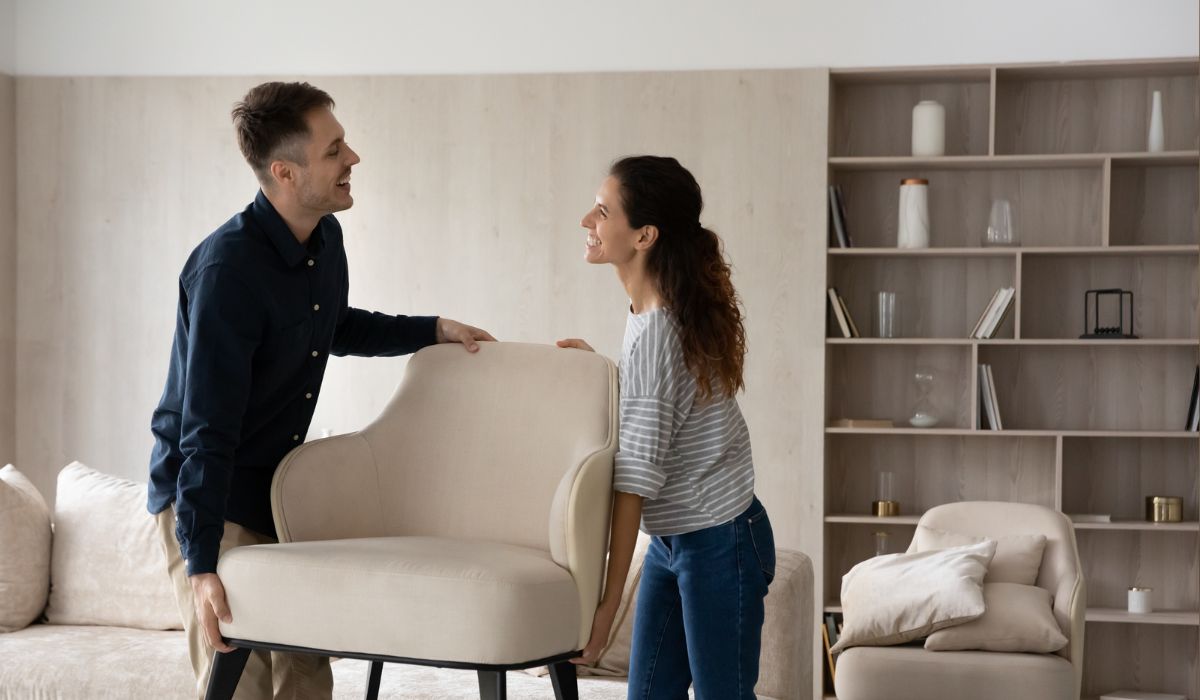 Junges Paar hebt gemeinsam einen Sessel im Wohnzimmer Junges Paar hebt gemeinsam einen Sessel im Wohnzimmer